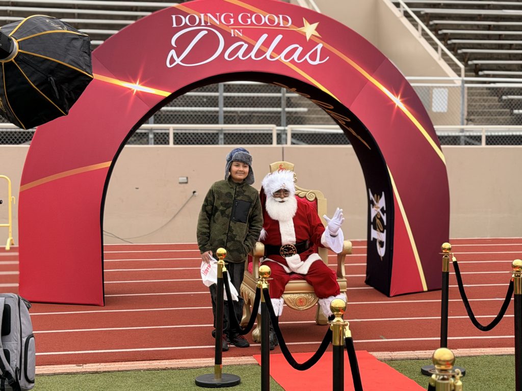 Student posing with Santa in front of Doing Good in Dallas backdrop