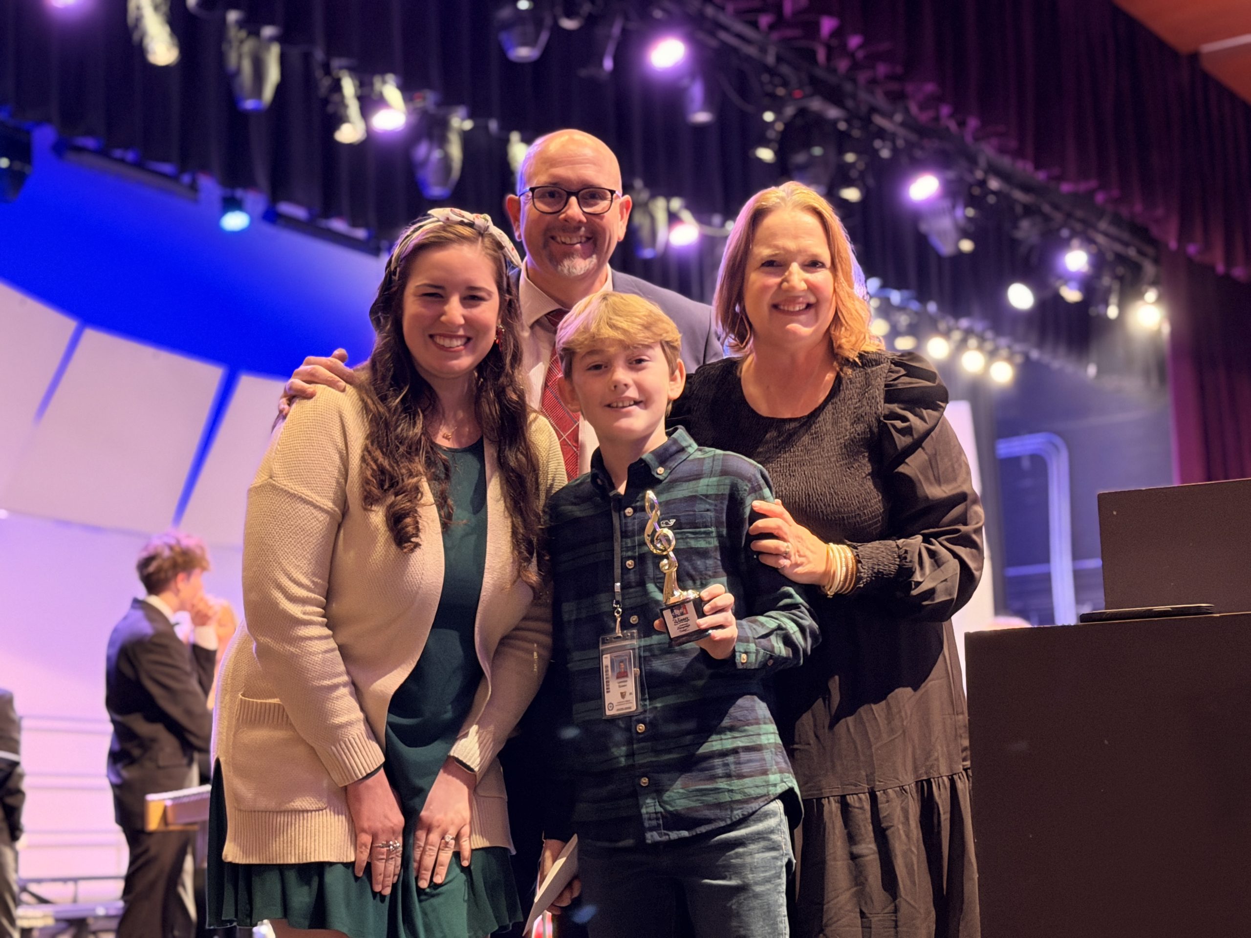 Student with trophy on stage with teacher and fine arts leadership staff