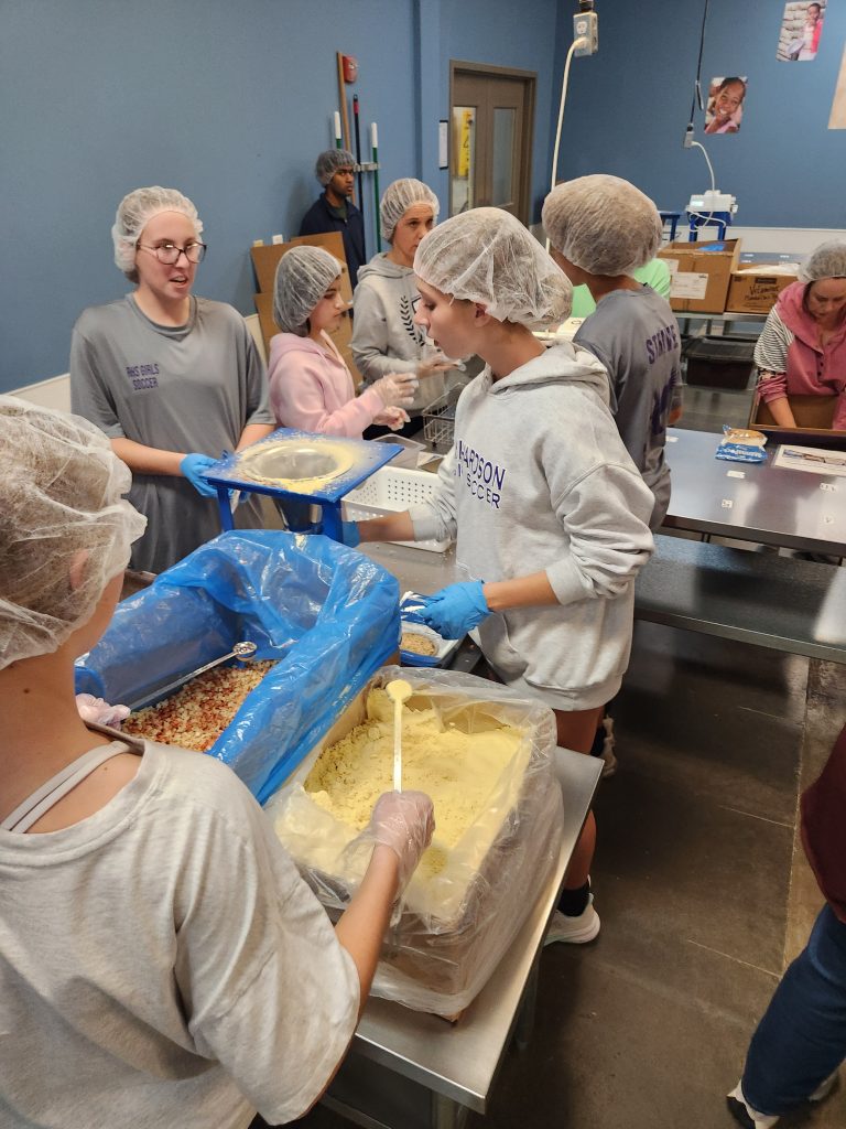 Female students measuring and weighing bulk food items for donation and distribution at local food bank