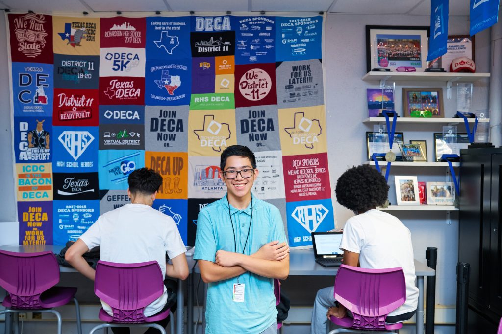 DECA Student in front of wall of deca shirts
