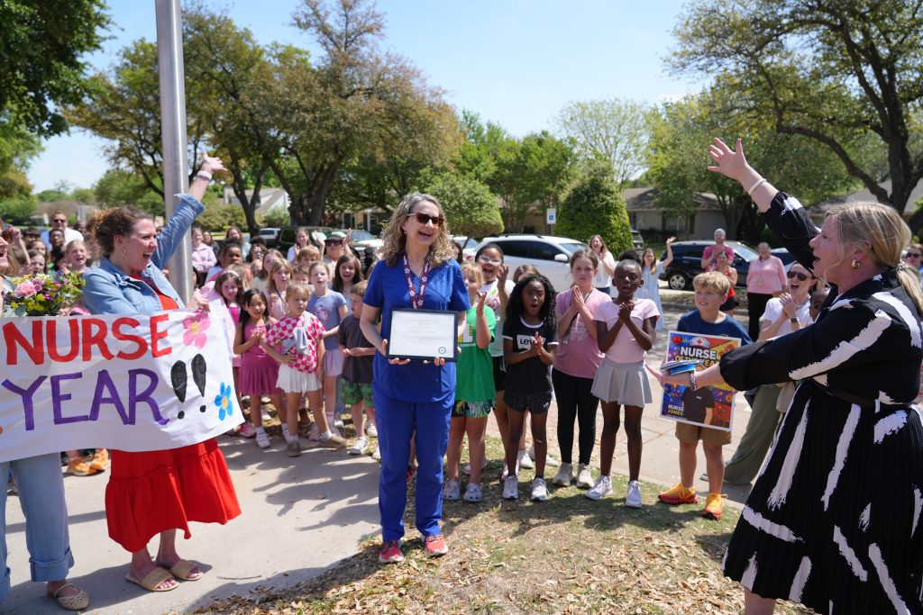Candid photo of Nurse Jones being surprised outside holding nurse of the year certificate surrounded by students