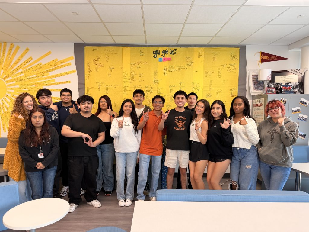 AVID Students holding up college hand signs in front of college acceptances wall