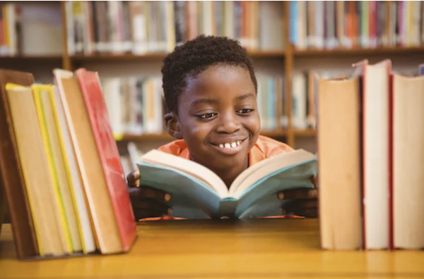 Boy smiling reading a book surrounded by books